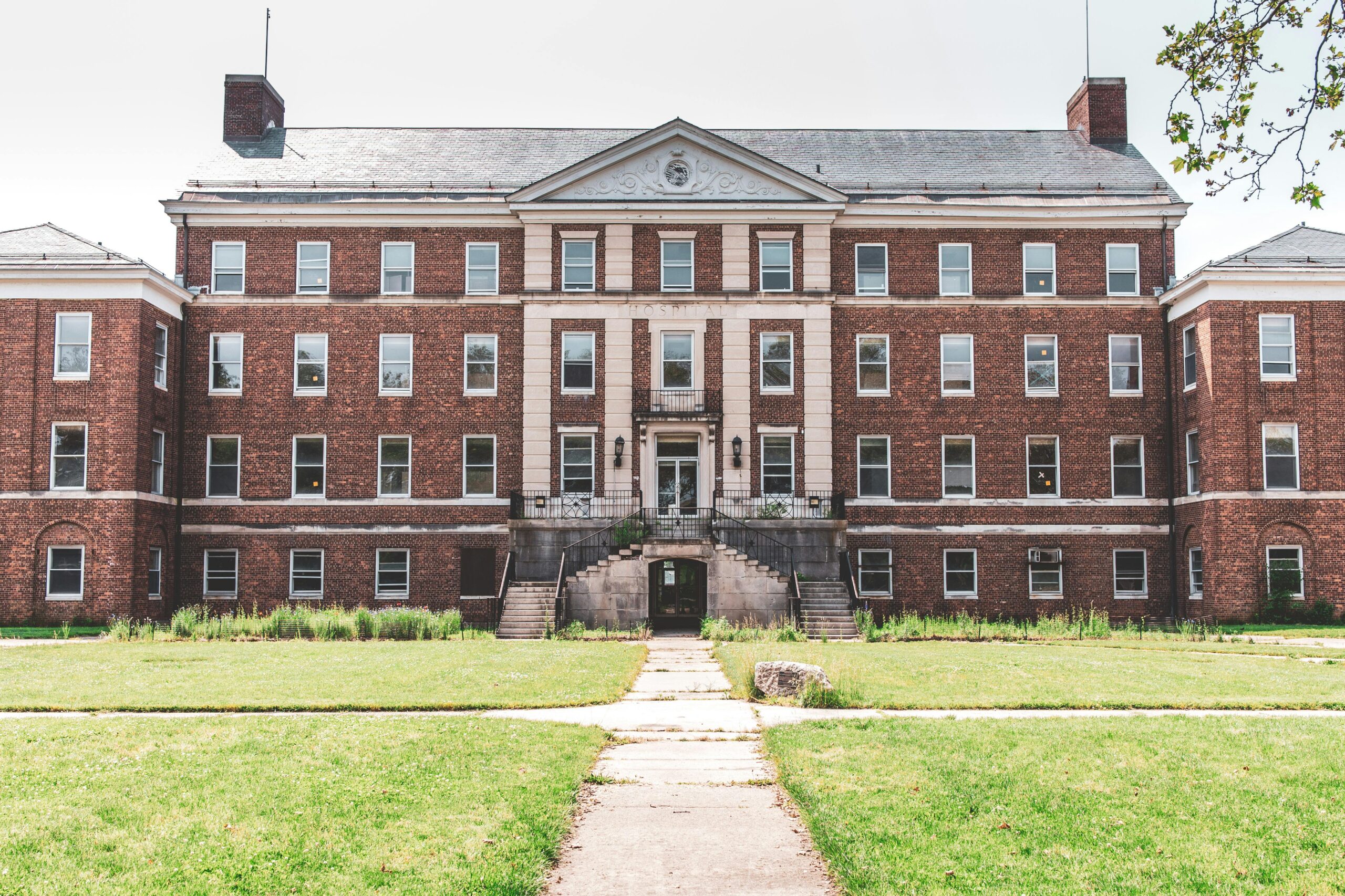 A historic brick building with classical elements, featuring a symmetrical facade and expansive lawn.